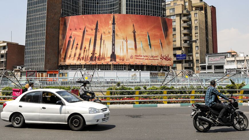 Motorists drive their vehicles past a billboard depicting named Iranian ballistic missiles in service, with text in Arabic reading, "The honest [person's] promise" and in Persian, "Israel is weaker than a spider's web," in Valiasr Square in central Tehran on April 15, 2024.